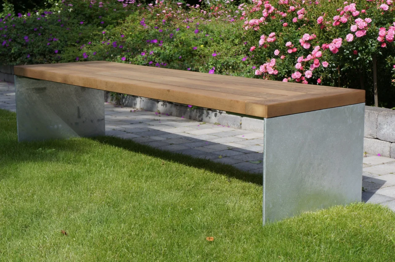 Sitzbank aus Holz und Metall in einem Garten oder Park umgeben von Gras und Blumen.