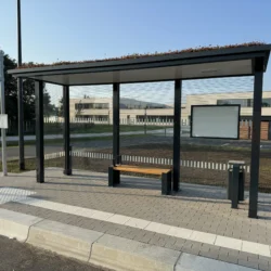 Wartehalle mit Gründach und Sitzbank an einer Bushaltestation vor einem größeren Gebäude.